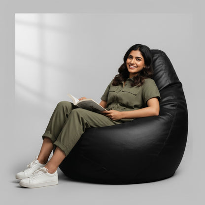 A smiling woman reading a book while sitting in a black tear-drop TipTop Retail bean bag cover on a grey background.