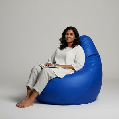 A woman sitting on a TipTop Retail ocean blue teardrop bean bag, reading a book in a comfortable, ergonomic position.
